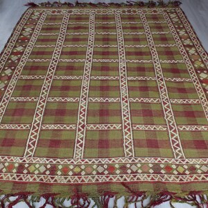 May include: A green and red woven rug with a geometric pattern. The rug has a fringe border.