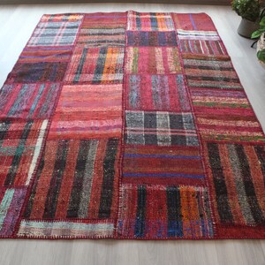 K&ouml;nnte beinhalten: Ein Patchwork-Teppich mit verschiedenen Farben und Mustern, darunter Rot, Schwarz und Wei&szlig;. Der Teppich ist aus gewebtem Stoff und hat einen Fransenrand.