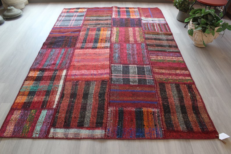 K&ouml;nnte beinhalten: Ein Patchwork-Teppich mit verschiedenen Farben und Mustern, darunter Rot, Schwarz und Wei&szlig;. Der Teppich ist aus gewebtem Stoff und hat einen Fransenrand.
