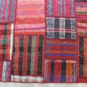 K&ouml;nnte beinhalten: Ein Patchwork-Teppich mit verschiedenen Farben und Mustern, darunter Rot, Schwarz und Wei&szlig;. Der Teppich ist aus gewebtem Stoff und hat einen Used-Look.