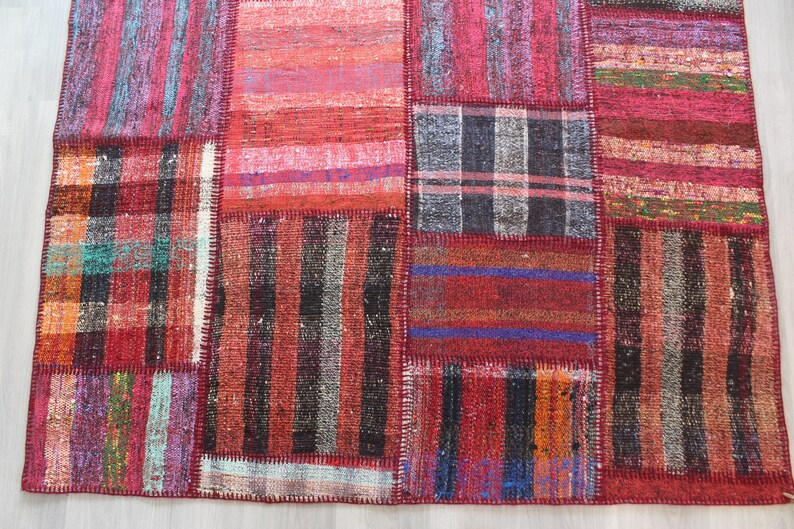 K&ouml;nnte beinhalten: Ein Patchwork-Teppich mit verschiedenen Farben und Mustern, darunter Rot, Schwarz und Wei&szlig;. Der Teppich ist aus gewebtem Stoff und hat einen Used-Look.