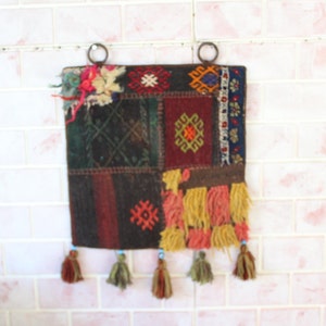 Peut inclure: Une tapisserie murale colorée avec un design patchwork présentant des motifs géométriques et des glands. La tapisserie est faite de tissu tissé et a un aspect rustique et vintage.
