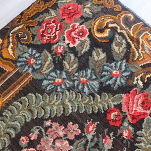 May include: A vintage rug with a floral pattern in shades of red, pink, green, and brown. The rug has a dark brown background with intricate details in the border.