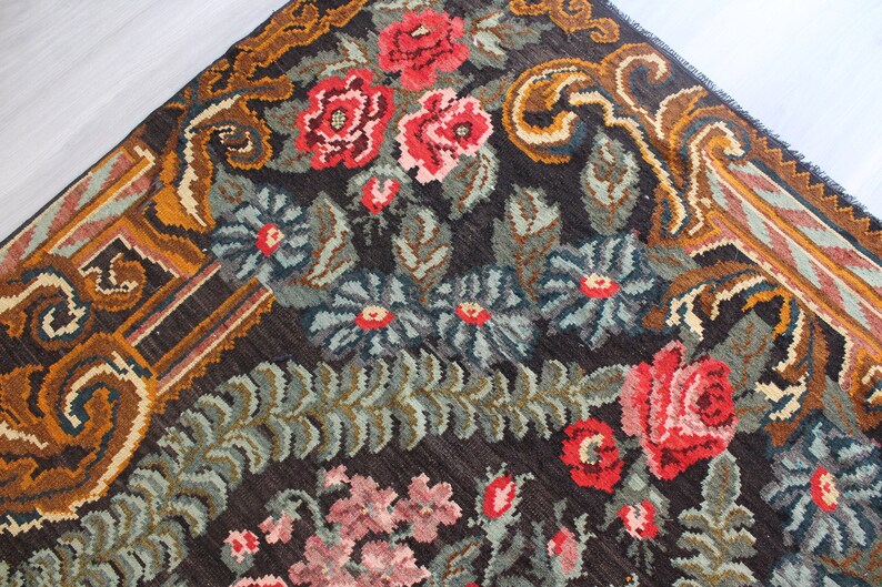 May include: A vintage rug with a floral pattern in shades of red, pink, green, and brown. The rug has a dark brown background with intricate details in the border.