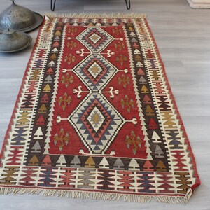 May include: A red, brown, white, and blue patterned rug with a geometric design. The rug has a fringe border.