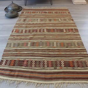 May include: A traditional Turkish kilim rug with a striped pattern in shades of brown, beige, and red. The rug has a fringe border and is woven with intricate geometric designs.