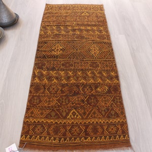 May include: A brown and gold runner rug with a geometric pattern. The rug has a fringe on both ends.