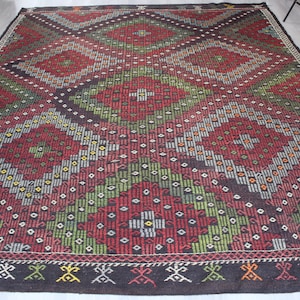 May include: A traditional Turkish rug with a geometric pattern in shades of red, green, black, and white. The rug has a diamond-shaped design with intricate details.