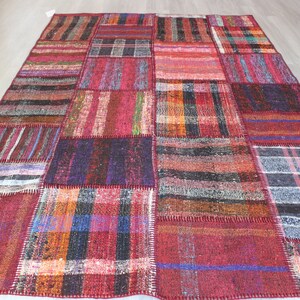 Op de afbeelding: Een patchwork tapijt met verschillende kleuren en patronen, waaronder rood, blauw, zwart en wit. Het tapijt is gemaakt van geweven stof en heeft een verweerde uitstraling.