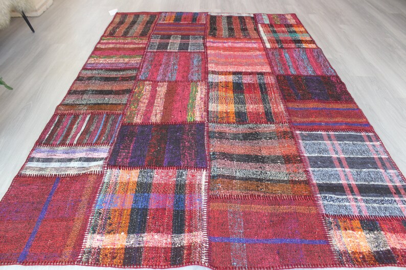K&ouml;nnte beinhalten: Ein Patchwork-Teppich mit verschiedenen Farben und Mustern, darunter Rot, Blau, Schwarz und Wei&szlig;. Der Teppich ist aus gewebtem Stoff und hat einen Used-Look.