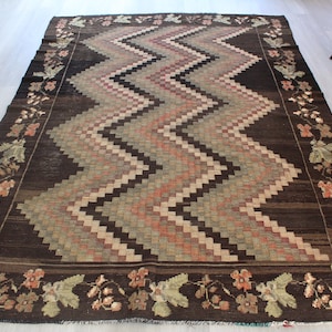 May include: A brown rug with a geometric pattern of zigzags and squares in shades of brown, pink, and green. The rug has a floral border.