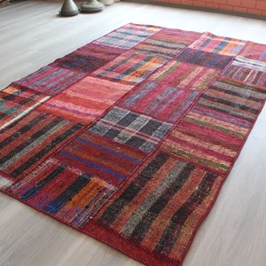 K&ouml;nnte beinhalten: Ein Patchwork-Teppich mit verschiedenen Farben und Mustern, darunter Rot, Schwarz und Wei&szlig;. Der Teppich ist aus gewebtem Stoff und hat einen Used-Look.