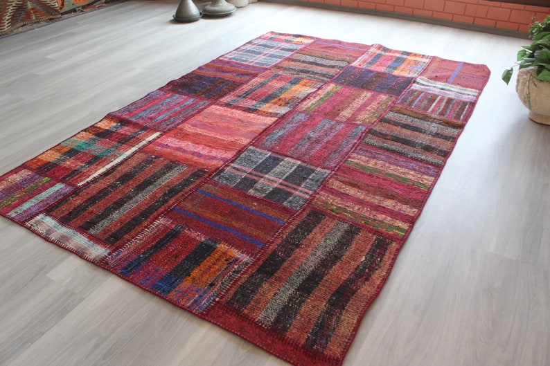 K&ouml;nnte beinhalten: Ein Patchwork-Teppich mit verschiedenen Farben und Mustern, darunter Rot, Schwarz und Wei&szlig;. Der Teppich ist aus gewebtem Stoff und hat einen Used-Look.