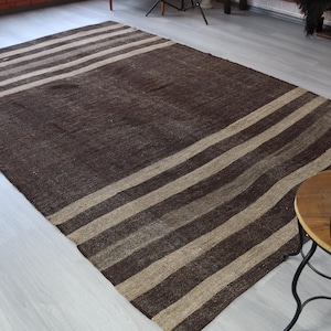 May include: A rectangular brown and beige striped rug. The rug has alternating wide stripes of dark brown and beige. The rug is made of a woven material and is placed on a light-colored wooden floor.