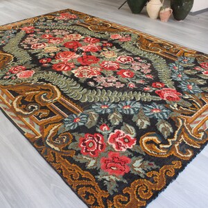 May include: A vintage floral rug with a black background and a central design of red, pink, and white flowers. The rug has a gold and brown border with intricate patterns.