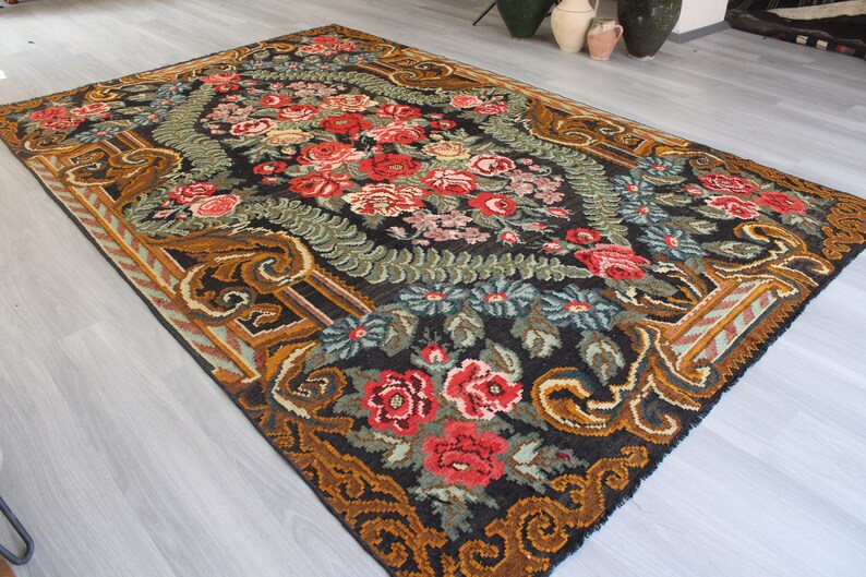 May include: A vintage floral rug with a black background and a central design of red, pink, and white flowers. The rug has a gold and brown border with intricate patterns.