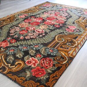 May include: A vintage floral rug with a dark brown background and a gold border. The rug features a repeating pattern of roses, leaves, and other floral motifs.