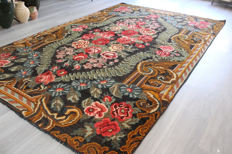 May include: A vintage floral rug with a dark brown background and a gold border. The rug features a repeating pattern of roses, leaves, and other floral motifs.