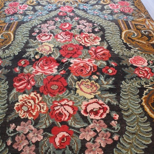 May include: A vintage rug with a floral pattern featuring red, pink, and white roses on a dark brown background. The rug has a border with a brown and gold design.