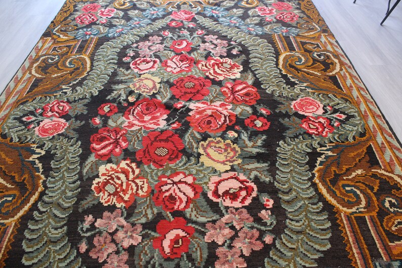 May include: A vintage rug with a floral pattern featuring red, pink, and white roses on a dark brown background. The rug has a border with a brown and gold design.