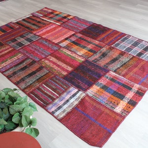 K&ouml;nnte beinhalten: Ein bunter Patchwork-Teppich mit verschiedenen Rot-, Blau- und Braunt&ouml;nen. Der Teppich ist aus gewebtem Stoff und hat eine rechteckige Form.