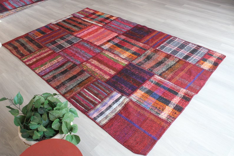 K&ouml;nnte beinhalten: Ein bunter Patchwork-Teppich mit verschiedenen Rot-, Blau- und Braunt&ouml;nen. Der Teppich ist aus gewebtem Stoff und hat eine rechteckige Form.