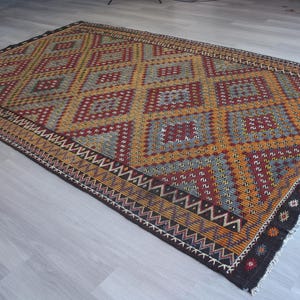 May include: A colorful rug with a geometric pattern in shades of red, orange, yellow, blue, and black. The rug has a diamond pattern with a black border.