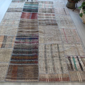 Può includere: Un tappeto patchwork con una varietà di colori e trame. Il tappeto è composto da diversi pezzi di tessuto cuciti insieme. Il tappeto è principalmente beige con accenti marroni, blu e rossi.