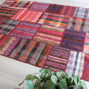 K&ouml;nnte beinhalten: Ein bunter Patchwork-Teppich mit verschiedenen roten, blauen und braunen Streifen und Mustern. Der Teppich ist aus gewebtem Stoff und hat einen abgenutzten, Vintage-Look.