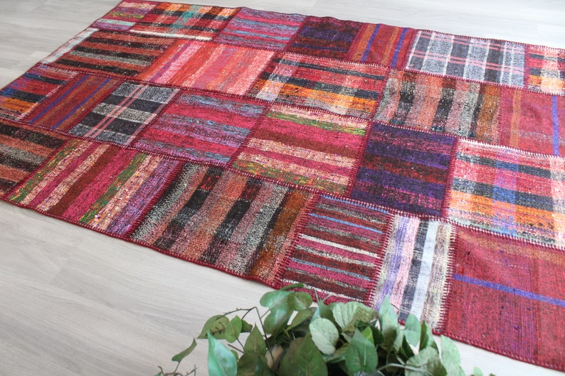 K&ouml;nnte beinhalten: Ein bunter Patchwork-Teppich mit verschiedenen roten, blauen und braunen Streifen und Mustern. Der Teppich ist aus gewebtem Stoff und hat einen abgenutzten, Vintage-Look.