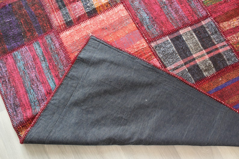 K&ouml;nnte beinhalten: Ein roter, blauer und grauer Patchwork-Teppich mit einer dunkelgrauen R&uuml;ckseite. Der Teppich besteht aus verschiedenen Stoffen und hat einen Fransenrand.