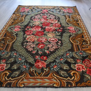 May include: A vintage floral rug with a dark brown background and a central design of red, pink, and white flowers. The rug has a border of gold and brown geometric patterns.
