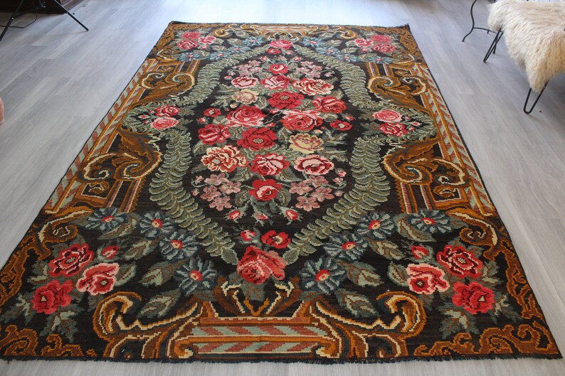 May include: A vintage floral rug with a dark brown background and a central design of red, pink, and white flowers. The rug has a border of gold and brown geometric patterns.