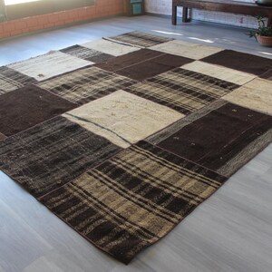 Puede incluir: Una alfombra de patchwork con una variedad de cuadrados marrones y beige. La alfombra está hecha de tejido tejido y tiene un aspecto rústico y vintage.