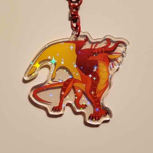 Peut inclure: Un porte-cl&eacute;s en acrylique transparent repr&eacute;sentant un dragon rouge et orange vif avec des ailes jaunes. Le motif est recouvert d'un effet d'&eacute;toiles holographiques qui refl&egrave;te la lumi&egrave;re, fix&eacute; &agrave; un anneau mousqueton en m&eacute;tal rouge.