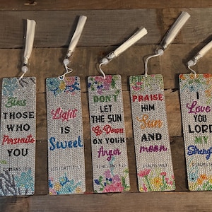 May include: A collection of seven rectangular bookmarks with inspirational quotes and floral designs. Each bookmark has a white tassel and features phrases like "Let Love Be Without Hypocrisy" and "I Love You Lord My Strength."