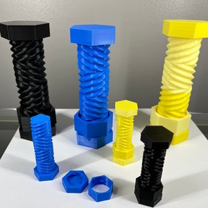 May include: Five 3D printed puzzle boxes in black, blue, and yellow. The boxes are shaped like nuts and bolts and have a spiral design. The boxes are open and show the inner workings of the puzzle.