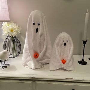 May include: Two white towel ghosts with googly eyes and orange pumpkin accents on a white dresser with three drawers.
