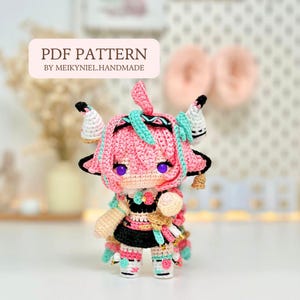 May include: A handmade crochet doll with pink hair, purple eyes, and a black and white outfit. The doll has small horns and is adorned with turquoise accents. The text "PDF PATTERN BY MEIKYNIEL.HANDMADE" is displayed above the doll.