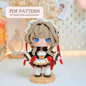 Op de afbeelding: Een gehaakte pop met lichtbruin haar, felblauwe ogen en een wit kanten hoofddeksel. De pop draagt een zwart-witte outfit met rode accenten, gouden details en witte sokken. De tekst PDF PATTERN BY MEIKYNIEL.HANDMADE is bovenaan zichtbaar.
