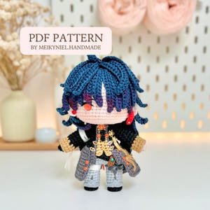 May include: A handmade crochet doll with blue hair and a detailed outfit. The doll has a peach-colored face and is wearing a black and gold jacket, gray pants, and gray boots. The text "PDF PATTERN BY MEIKYNIEL.HANDMADE" is displayed on a white banner.