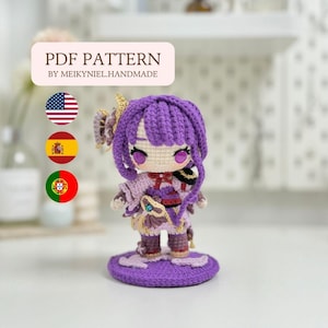 Puede incluir: Patrón de crochet PDF para una muñeca de personaje de anime morado y dorado. La muñeca está de pie sobre una base morada. El patrón está disponible en inglés, español y portugués.