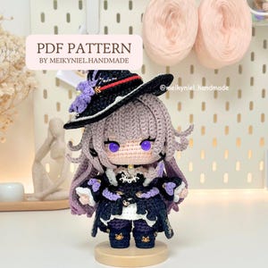 Op de afbeelding: Een handgemaakte gehaakte pop met een heksenachtig uiterlijk, met een zwarte hoed met paarse accenten, een zwart-paarse jurk en lavendelkleurig haar. De pop heeft grote paarse ogen. De tekst op de afbeelding luidt "PDF PATTERN BY MEIKYNIEL.HANDMADE".