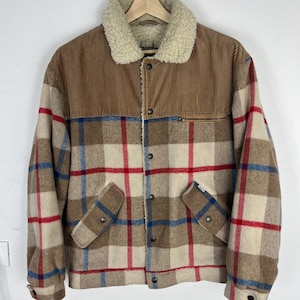 Può includere: Giacca a quadri marrone e beige con pannello superiore in velluto a coste e colletto in montone color crema. La giacca ha una chiusura con bottoni, due tasche frontali e una tasca con zip sul petto.