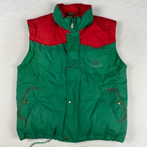 Könnte beinhalten: Grün-rote Steppweste mit Reißverschluss und Druckknöpfen. Die Weste hat ein Logo mit der Aufschrift "Trappers Look" und einem Ahornblatt.