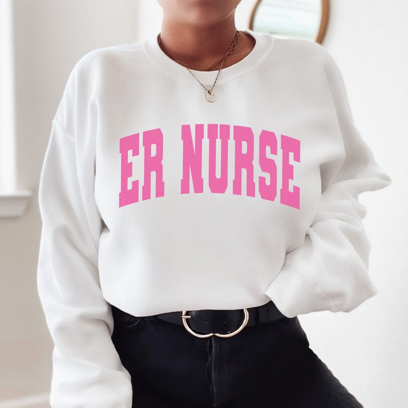 May include: White sweatshirt with pink text that reads "ER NURSE" in a collegiate font.