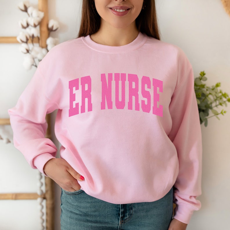 May include: Pink sweatshirt with the text "ER NURSE" in a large, white font.