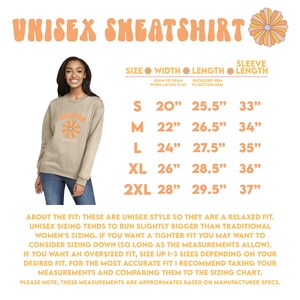 May include: A unisex sweatshirt in a light beige color with a flower graphic and the text "Grateful" in a retro font. The image also shows a size chart with measurements in inches for width, length, and sleeve length.