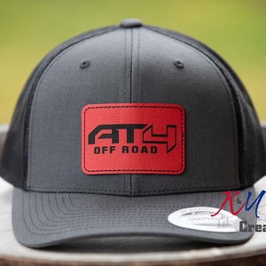 May include: A gray and black trucker hat with a red patch that says "AT4 OFF ROAD" in black lettering.