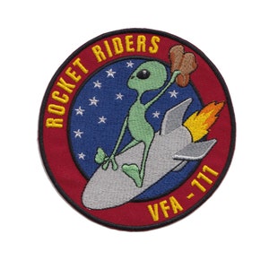 May include: A red, white, and blue embroidered patch with a green alien riding a rocket. The text "ROCKET RIDERS" is in yellow lettering around the top of the patch. The text "VFA-177" is in yellow lettering at the bottom of the patch.
